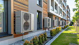 Außenansicht eines modernen Apartmenthauses mit mehreren Außeneinheiten von Klimaanlagen.